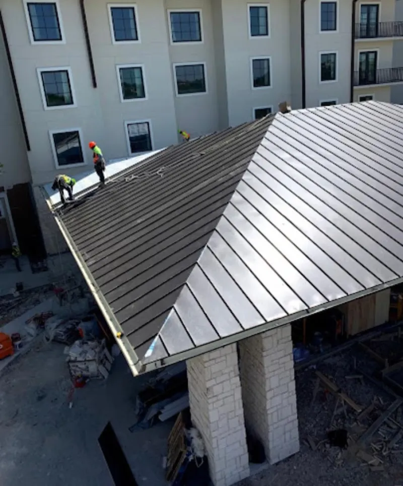 Crew installing standing seam metal roof panels on a commercial project in Monroe